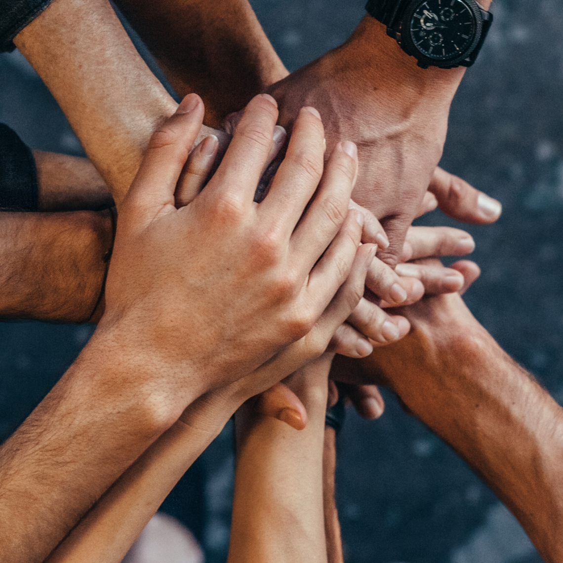 People placing their hands atop one another with a view of the ground