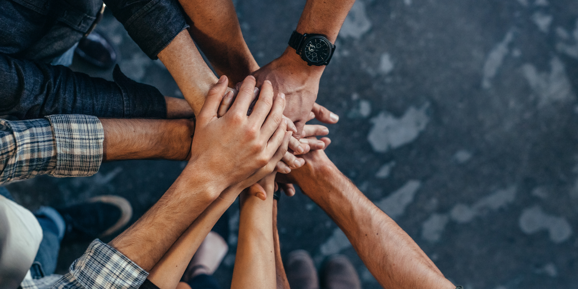 People placing their hands atop one another with a view of the ground